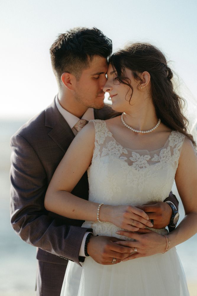 A bride and groom standing forehead to forehead in a grassy mountain field